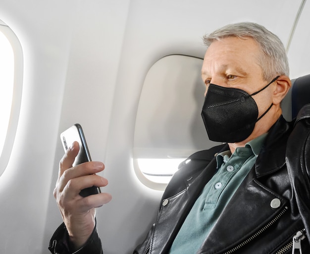 Homme portant un masque facial et utilisant un téléphone dans la cabine de l'avion pendant le vol