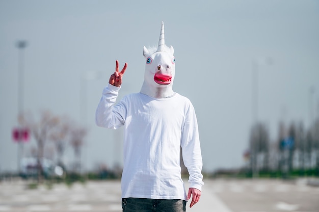 Photo homme portant un masque de licorne faisant le geste de la victoire avec les doigts