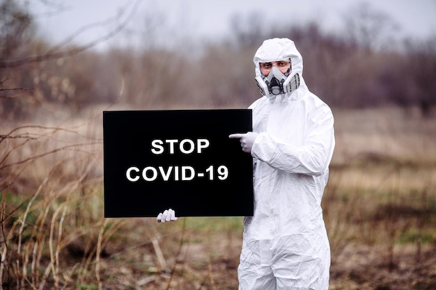 Homme portant un masque médical et une combinaison de protection avec une affiche dans les mains Concept épidémique et médical