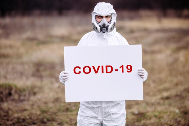 Homme portant un masque médical et une combinaison de protection avec une affiche dans les mains Concept épidémique et médical