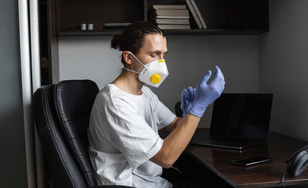 L'homme portant un masque médical porte des gants en caoutchouc à son lieu de travail à la maison pendant la quarantaine