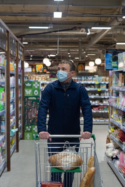 Un homme portant un masque protecteur choisit des marchandises dans un supermarché Commerce de détail Quarantaine