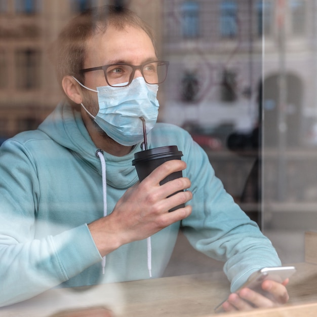 Homme portant un masque de protection, boire du café à travers une paille dans un masque au café