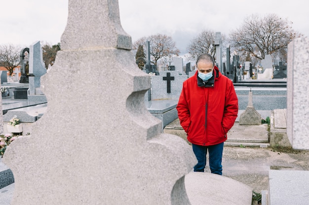 Homme portant un masque, triste et priant, devant la tombe d'un parent décédé en période de covid-19