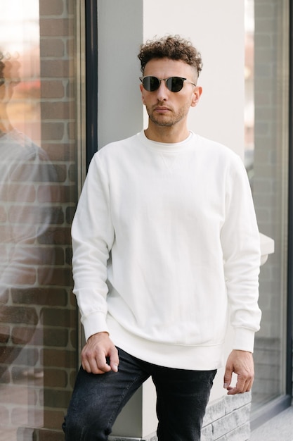 Homme portant un sweat-shirt ou un sweat à capuche blanc pour des maquettes de logos ou des impressions de conception avec de l'espace libre dans les rues de la ville