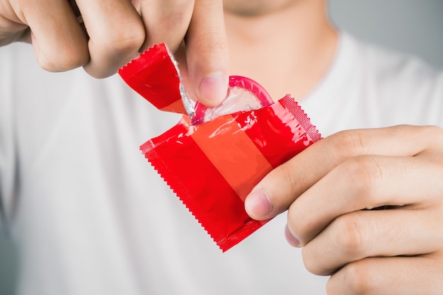 Homme portant un t-shirt blanc et main déchirant un préservatif rouge