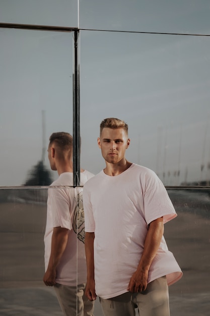 Homme portant un t-shirt blanc posant contre le mur de miroir de verre dans la rue de la ville, maquette de tshirt avant sur modèle, style urbain