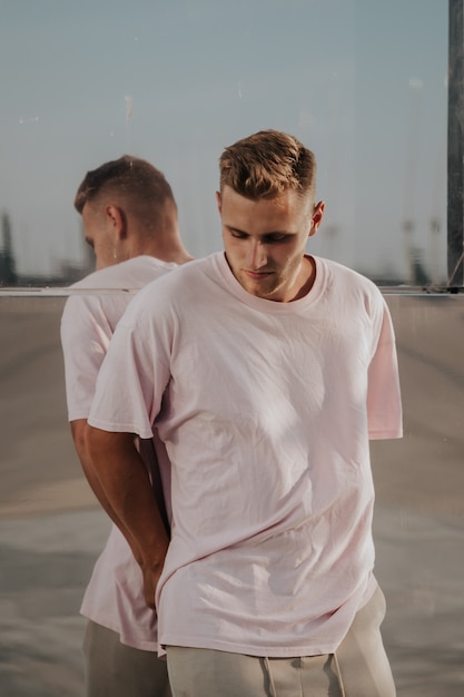 Homme portant un t-shirt blanc posant contre le mur de miroir de verre dans la rue de la ville, maquette de tshirt avant sur modèle, style urbain