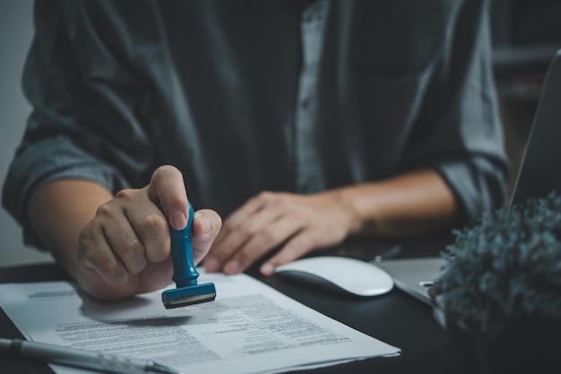 Photo homme portant le timbre d'approbation à la main signant un document ou un contrat de paperasse au bureau