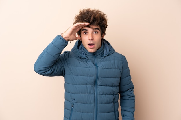 Photo homme portant une veste d'hiver sur un mur isolé avec surprise et expression faciale choquée