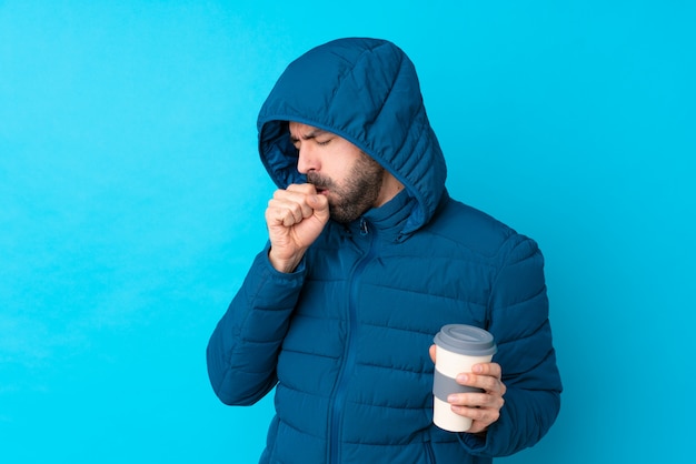 Homme portant une veste d'hiver et tenant un café à emporter sur le mur bleu isolé souffre de toux et se sent mal