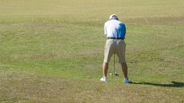 Photo un homme porte une chemise bleue et des khakis sur le point de frapper une balle de golf au milieu d'une pelouse verte