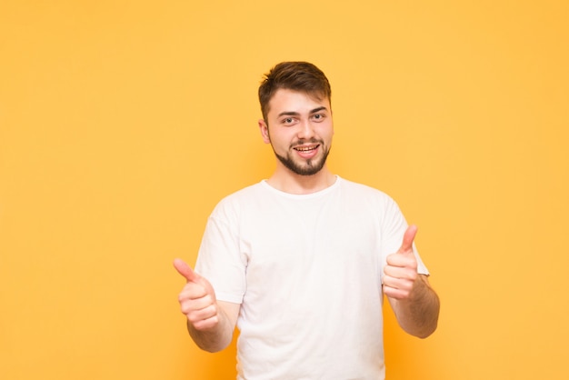 L'homme porte un T-shirt blanc, montre un coup de pouce et regarde la caméra, isolé sur un jaune