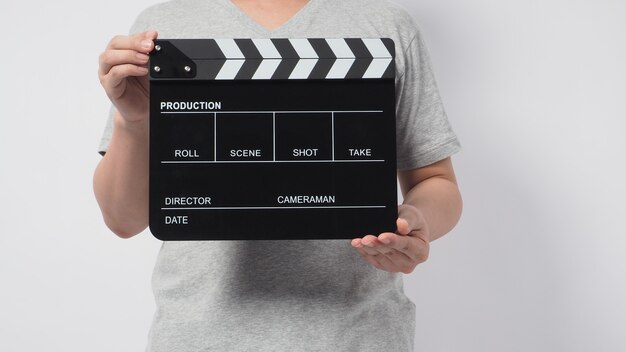 Un homme porte un t-shirt gris et la main tient un tableau noir Clapper ou une ardoise de film. il est utilisé dans la production vidéo ou l'industrie du cinéma. C'est un fond blanc.