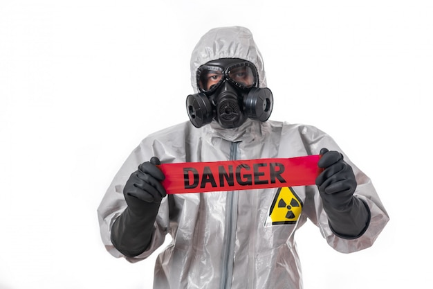 Un homme pose dans une combinaison de protection grise avec un capuchon sur la tête, avec un masque à gaz protecteur, posant en se tenant debout sur un fond blanc, tenant un ruban de danger rouge dans ses mains. Ruban de danger. Protection.