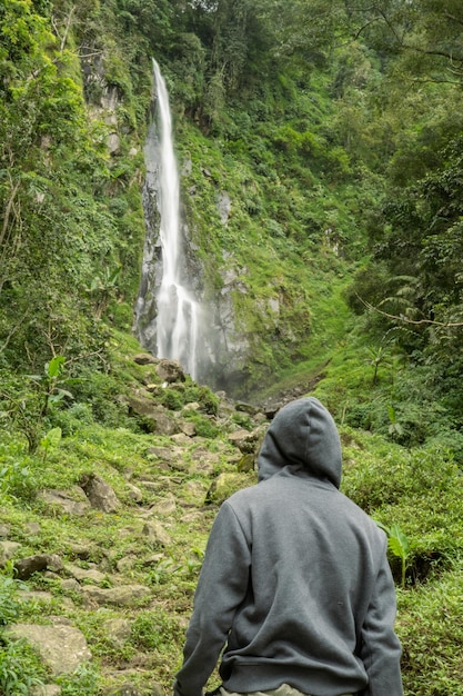 L'homme pose devant la haute chute d'eau sur la forêt tropicale