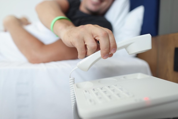 Un homme pose le téléphone alors qu'il était allongé dans son lit dans une commande de service de villégiature floue gros plan de l'hôtel