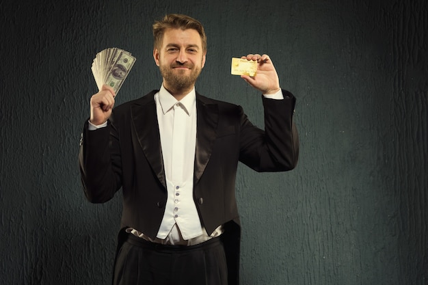 L'homme positif dans un tailcoat offre une carte de crédit et de l'argent.