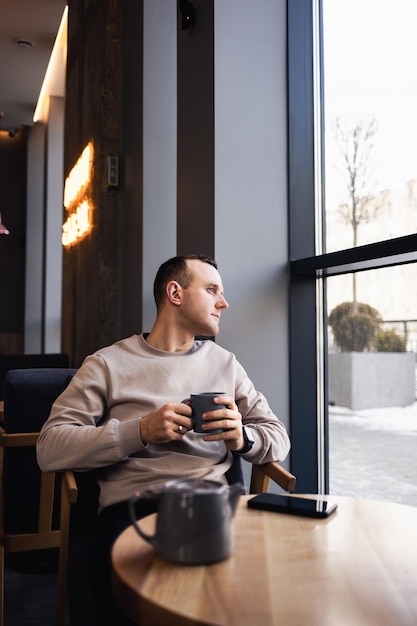 Un homme positif est assis dans un café à une table, il boit du café aromatique Un gars souriant en vêtements décontractés est assis dans un café et boit du café le matin