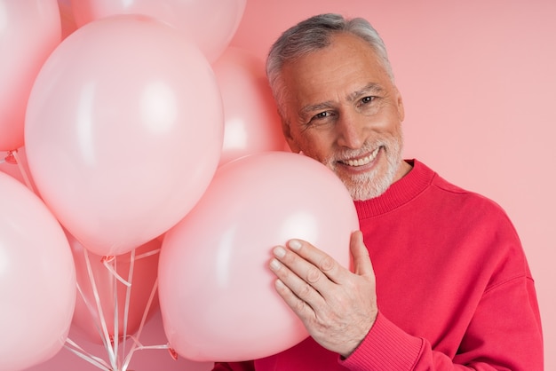 Homme positif et joyeux avec des ballons posant sur un mur rose