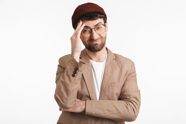 homme positif portant un chapeau hipster souriant et touchant son front isolé sur un mur blanc