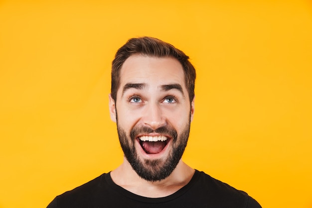 homme positif en t-shirt noir de base riant et regardant vers le haut isolé sur un mur jaune