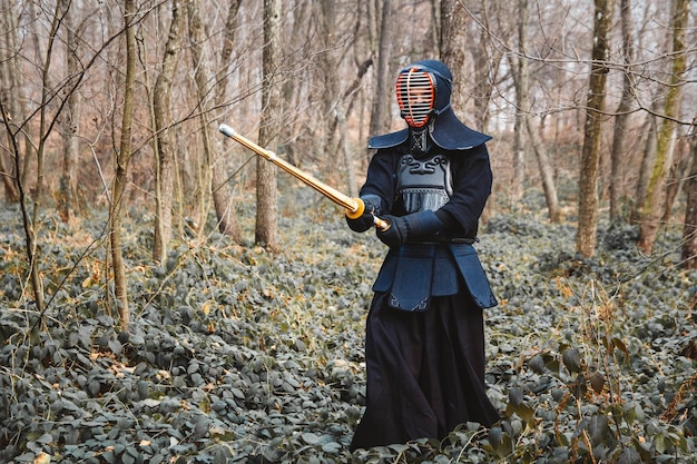 Homme pratiquant le kendo avec épée de bambou shinai sur fond de forêt. Place pour le texte ou la publicité