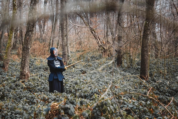 Homme pratiquant le kendo avec épée de bambou shinai sur fond de forêt