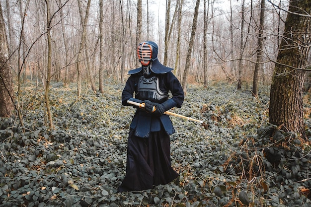 Homme pratiquant le kendo avec épée de bambou shinai sur fond de forêt