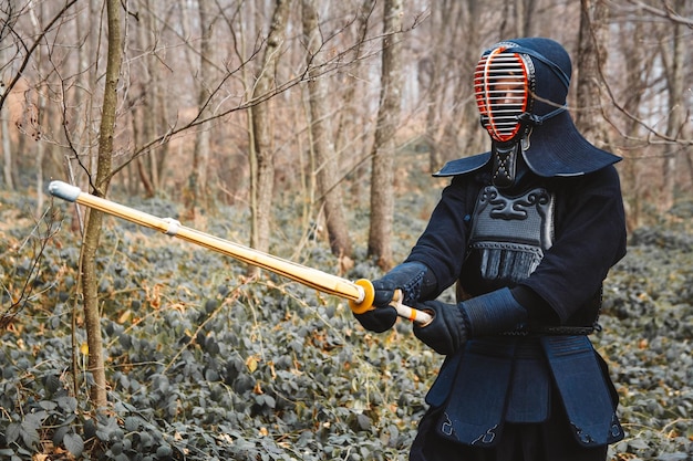 Homme pratiquant le kendo avec épée de bambou shinai sur fond de forêt