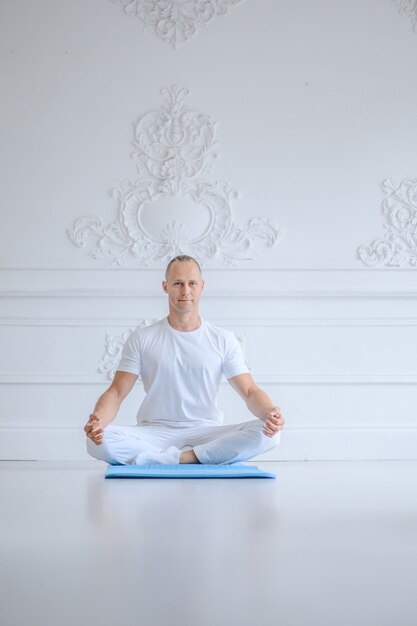 Homme pratiquant le yoga avancé contre un mur blanc