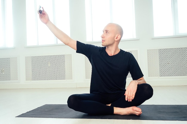 L'homme pratique le yoga et fait du selfie au téléphone dans le studio. asanas du matin en cours de yoga