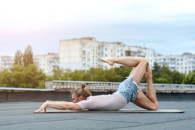 Un homme pratique le yoga sur le toit de la maison. Yoga au coucher du soleil. Concept de vie saine, de sport et de méditation.