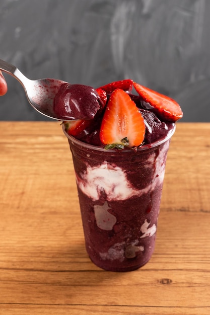 Homme prenant une cuillerée de smoothie brésilien surgelé à la crème glacée aux baies d'Açai dans une tasse en plastique avec des fraises et du lait concentré. Sur fond d'été. Vue de face pour le menu et les médias sociaux