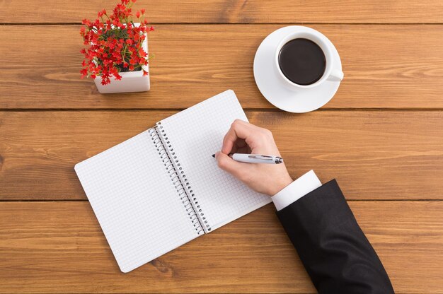 Homme prenant des notes assis à une table en bois, gros plan, vue de dessus.