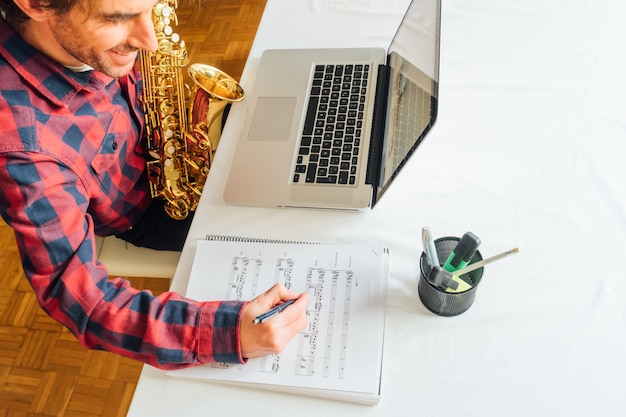 Homme prenant des notes sur des partitions tout en prenant son cours en ligne de saxophone