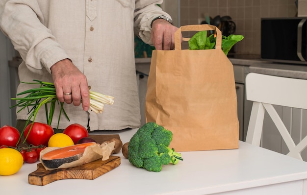 Homme prenant de la nourriture dans un sac en papier Légumes et légumes verts dans un sac en papier sur la table de la cuisine