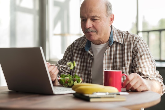Homme prenant un petit-déjeuner sain assis à la table de la cuisine avec un ordinateur portable