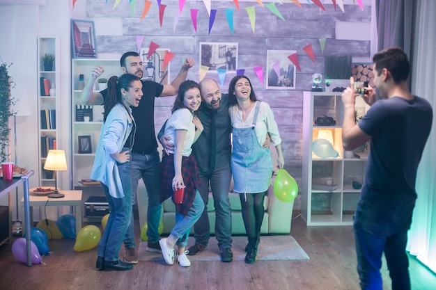 Homme prenant des photos d'amis riant lors d'une fête dans un appartement.