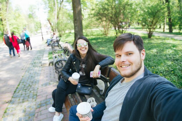 Homme prenant selfie dans le parc de la ville assis sur un banc jeune femme élégante sur fond