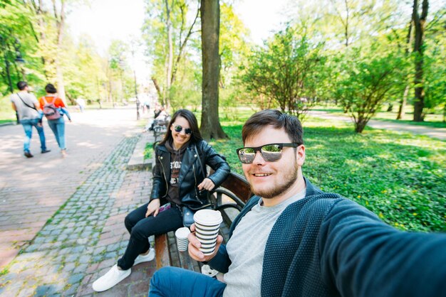 Homme prenant selfie dans le parc de la ville au banc jeune adulte sur fond