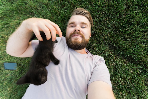 Homme prenant selfie avec smartphone avec petit chaton allongé et jouant sur l'herbe amitié amour animaux et concept de propriétaire d'animal