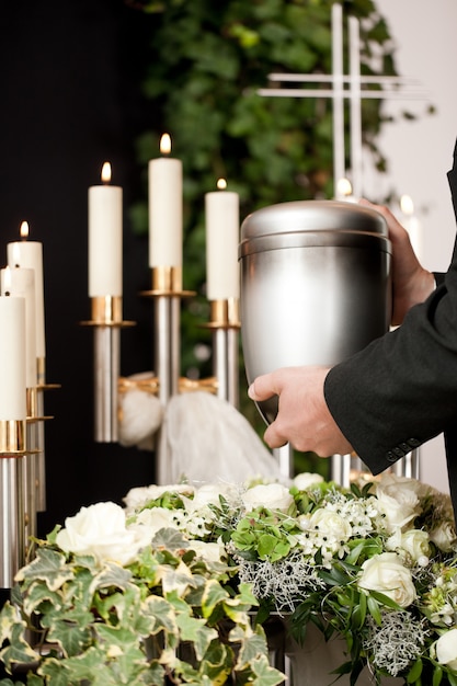 homme prenant l'urne funéraire avec des bougies et des fleurs