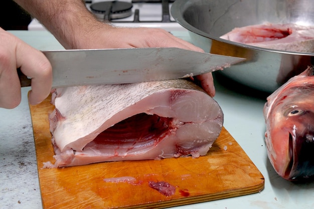 Un homme prépare du poisson de carpe argentée frais et le coupe en steaks avec un couteau.