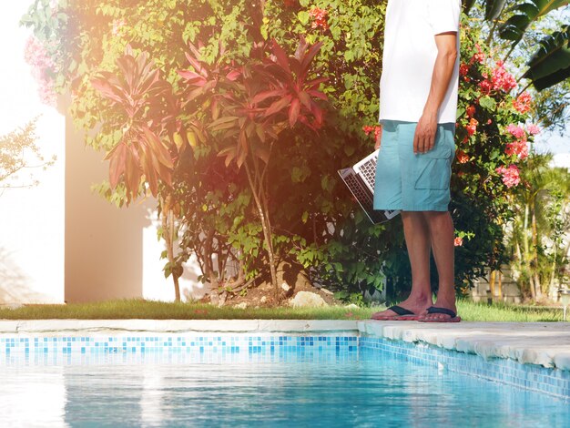 Homme près d'une piscine avec un ordinateur portable