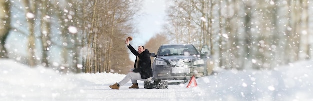 Un homme près d'une voiture cassée un jour d'hiver