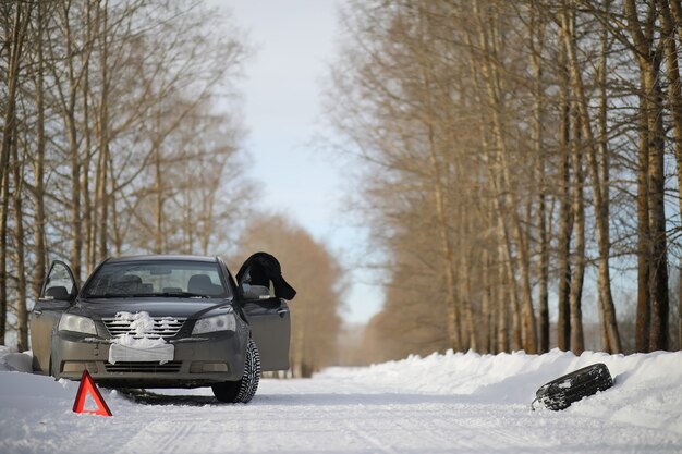 Un homme près d'une voiture cassée par une froide journée d'hiver