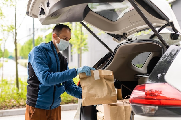 L'homme près de la voiture. Guy dans un uniforme de livraison. Homme dans un masque médical. Notion de coronavirus.