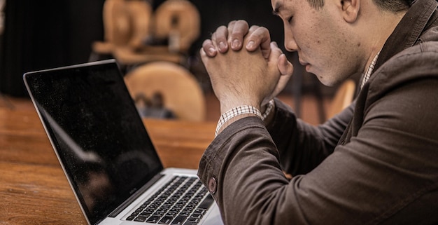 Photo un homme priant par la foi avec un ordinateur portable, le concept en ligne des services de l'église, l'église en ligne à la maison