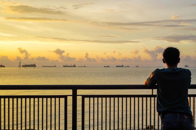 Photo un homme profite de la vue du coucher de soleil et d'une rangée de navires de cargaison à voile